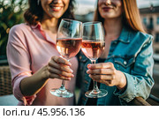 Glasses of pink sparkling wine in the hands of people. People are relaxing on the outdoor veranda. The concept of recreation, corporate event, party or celebration. Стоковое AI-изображение, AI-художник Photojuli / Фотобанк Лори