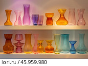 Colorful glass vases and drinking glasses displayed on shelves creating a vibrant arrangement. Стоковое AI-изображение, AI-художник Иван Рябоконь / Фотобанк Лори