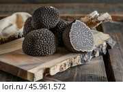 Black truffles showing cross section on rustic wooden board. Стоковое AI-изображение, AI-художник Иван Рябоконь / Фотобанк Лори
