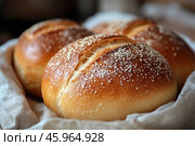 Three delicious buns with golden crusts lying on a light cloth. The pastries look fresh and homemade, with a perfectly baked surface covered with a crispy crust and sprinkled with small seeds or flour. The buns are placed close to each other, creating a feeling of coziness and homely warmth. The light falls softly on the pastries, emphasizing their texture and golden hue. The cloth on which the buns are lying adds an element of coziness and emphasizes the rustic style of the image.This scene brings to mind cozy kitchen mornings, the smell of freshly baked bread and the warmth of a home. Attention to detail, such as the texture of the crust and the soft folds of the fabric, creates a sense of quality and care put into the baking process. Стоковое AI-изображение, AI-художник Анна Кривицкая / Фотобанк Лори