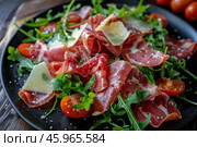 Delicious coppa ham salad with arugula, cherry tomatoes and parmesan cheese shavings. Стоковое AI-изображение, AI-художник Иван Рябоконь / Фотобанк Лори
