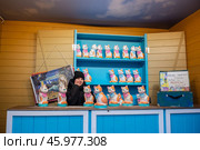 Россия, Москва, Площадь Революции - Январь 2025. Девочка за прилавком с кошками - копилками на рынке. Декорации из фильма Леонида Гайдая "Операция "Ы" и другие приключения Шурика. Фотозона. Russia, Moscow, Revolution Square - January 2025. The girl behind the counter with the piggy bank cats at the market. Scenery from Leonid Gaidai's film "Operation Y" and other adventures of Shurik. The photo zone. Стоковое фото, фотограф Мария / Фотобанк Лори