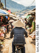 Vietnamese man riding bicycle wearing conical hat at bac ha market. Стоковое AI-изображение, AI-художник Юрий Поздников / Фотобанк Лори