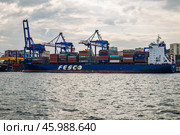 Vladivostok, Russia - August 9, 2021: Cargo cranes loading colorful containers in the port of vladivostok, russia, with the zolotoy rog bridge in the background. Редакционное фото, фотограф Mikhail Davidovich / Фотобанк Лори