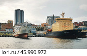 Vladivostok, Russia - August 9, 2021: Icebreaker and cargo ship docked in vladivostok harbor, showcasing maritime activity against a cityscape backdrop. Редакционное фото, фотограф Mikhail Davidovich / Фотобанк Лори