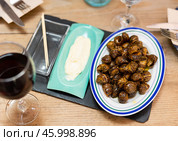 Snail dish, served on a ceramic plate with white sauce, glass of red wine close to the fork and chopsticks. Стоковое фото, фотограф Яков Филимонов / Фотобанк Лори