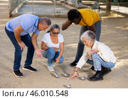 Positive mature diverse percioners comparing the distance of pumped balls after petangue at the sunny afternoon outdoors. Стоковое фото, фотограф Яков Филимонов / Фотобанк Лори