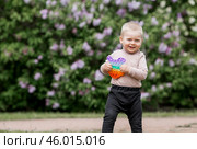 A beautiful chubby 2-year-old child in the park with a colorful Pop-it game. An anti-stress remedy. A pop It toy in children's hands. Стоковое фото, фотограф Photojuli / Фотобанк Лори
