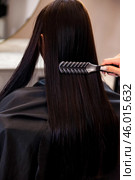 Hands of hairstylist combing black long hair of brunette woman at mirror in barber shop, close-up. Hairdresser makes fashionable hairstyle. Customer service at hair salon, haircare. Copy ad text space. Стоковое фото, фотограф Aleksandr Golubev / Фотобанк Лори