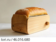 Loaf of freshly baked bread resting in wooden breadbox on white background. Стоковое AI-изображение, AI-художник Иван Рябоконь / Фотобанк Лори