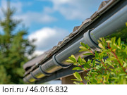 Rain gutter system protecting house roof from water damage on sunny day. Стоковое AI-изображение, AI-художник Иван Рябоконь / Фотобанк Лори