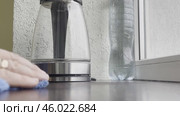 A man's hand wipes drops of water on the windowsill near the electric kettle with a blue cloth. Стоковое видео, видеограф Ярославский Максим / Фотобанк Лори