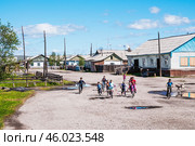 Сельская местность, дома, улица после дождя, дети на велосипедах, детские игры на улице. Поселок Томтор в Якутии ( Республика САХА, Оймяконский район ). Это очень удаленное место от Большой Земли, и жизнь здесь течет неторопливо (2010 год). Редакционное фото, фотограф Павел Просянов / Фотобанк Лори
