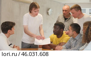 Focused young guy student holding papers ad discussing assignments or projects with interested male group of various ages and nationalities gathered around table in classroom. Стоковое видео, видеограф Яков Филимонов / Фотобанк Лори