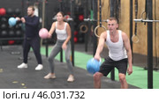 Sporty young adult man exercising with kettlebell to strengthen body muscles in modern gym during group workout. Physical activity and bodybuilding concept. Стоковое видео, видеограф Яков Филимонов / Фотобанк Лори