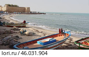 Traditional fishing boats resting on sandy shore Mediterranean Sea in Tunisian town of of Hammamet with sturdy stone historical walls of Kasbah in background. Стоковое видео, видеограф Яков Филимонов / Фотобанк Лори