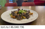 Warm salad with chicken liver in cream sauce with fried potatoes, mushrooms and mixed green salad in a white porcelain plate on a brown wooden table in an elite restaurant. Стоковое видео, видеограф worker / Фотобанк Лори