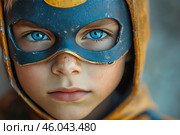 Portrait of a child wearing a superhero mask. The boy has bright blue eyes, freckles and a slightly serious expression. The mask, made in blue and gold, looks aged and worn, which adds a sense of realism and depth. His gaze is directed straight into the lens, creating a strong effect of involvement and emotional expressiveness.The overall impression of the image is inspirational, courageous and dreamy. It conveys the atmosphere of a child's imagination, the desire to be a hero, strong and special. Стоковое AI-изображение, AI-художник Анна Кривицкая / Фотобанк Лори