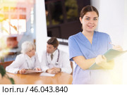 positive young medical female colleague standing in meeting room and employees are talking behind her at table. Стоковое фото, фотограф Яков Филимонов / Фотобанк Лори