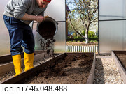A male farmer pours new soil, soil for a new greenhouse. The concept of spring vegetable planting, greenhouse installation and farming. Стоковое фото, фотограф Photojuli / Фотобанк Лори
