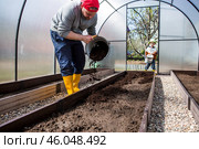 A male farmer pours new soil, soil for a new greenhouse. The concept of spring vegetable planting, greenhouse installation and farming. Стоковое фото, фотограф Photojuli / Фотобанк Лори