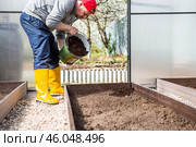 A male farmer pours new soil, soil for a new greenhouse. The concept of spring vegetable planting, greenhouse installation and farming. Стоковое фото, фотограф Photojuli / Фотобанк Лори