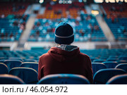 Spectator wearing beanie watching event in stadium bleachers. Стоковое AI-изображение, AI-художник Иван Рябоконь / Фотобанк Лори