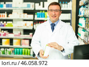 Portrait of friendly man druggist in lab coat standing in drugstore with drug package. Стоковое фото, фотограф Яков Филимонов / Фотобанк Лори