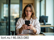 Upset woman looking at smartphone in office, worried about scam or fraud, serious expression, modern workplace, frustrated and stressed mood. Стоковое AI-изображение, AI-художник Павел Муравьев / Фотобанк Лори