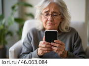 Elderly woman worriedly looking at smartphone, upset after phone scam, feeling sad and confused, financial loss, sitting on chair indoors. Стоковое AI-изображение, AI-художник Павел Муравьев / Фотобанк Лори