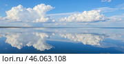 Stunning view of large white clouds mirrored in still water, bright blue sky above, perfect symmetry, natural beauty, idyllic and relaxing atmosphere. Стоковое AI-изображение, AI-художник Павел Муравьев / Фотобанк Лори