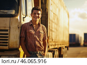 Young Latino truck driver, around 20, smiling by his vehicle at sunny freight yard. Стоковое AI-изображение, AI-художник Владимир Григорьев / Фотобанк Лори