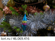 Новогодняя рождественская игрушка висит на ветке новогодней елки,  окутанная блестящей мишурой New Year's Christmas toy hangs on a New Year's tree branch, covered in shiny tinsel. Стоковое фото, фотограф Юрий Карачев / Фотобанк Лори
