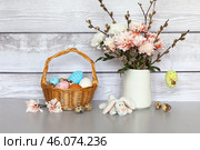 Easter rustic still life with spring bouquet of pussy willow branches and pink chrysanthemums, traditional painted Easter eggs in wicker basket and toy Easter bunny on grey table. Стоковое фото, фотограф Виктория Катьянова / Фотобанк Лори