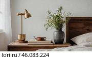 Cozy bedroom corner with warm lighting, a vase of flowers, and a cup of coffee on a wooden nightstand. Стоковое AI-изображение, AI-художник Сергей Толмачёв / Фотобанк Лори