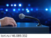 Male hand with microphone on podium of conference hall background, public speaking concept. Стоковое AI-изображение, AI-художник Евгений Харитонов / Фотобанк Лори