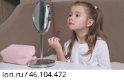Fashion little girl in a white T-shirt is sitting at the dressing table in front of the mirror and applying makeup with face powder. Advertising of children's cosmetics concept. Footage for kids blog. Стоковое видео, видеограф Ирина Михайличенко / Фотобанк Лори