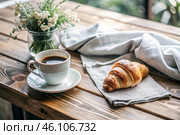 A delicious freshly baked croissant, a white cup of coffee and a cotton napkin on a wooden background. French breakfast. Delicious pastries in close-up. Стоковое AI-изображение, AI-художник Photojuli / Фотобанк Лори