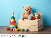 Wooden box with children's toys. A container with a teddy bear and educational wooden toys on a light blue background. Стоковое AI-изображение, AI-художник Photojuli / Фотобанк Лори