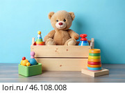 Wooden box with children's toys. A container with a teddy bear and educational wooden toys on a light blue background. Стоковое AI-изображение, AI-художник Photojuli / Фотобанк Лори