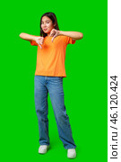 Young woman expressing disapproval in a bright orange shirt against a green background during a casual indoor setting. Стоковое фото, фотограф Сергей Толмачёв / Фотобанк Лори