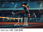 Athlete hurdles over a barrier during a sunset track and field competition in an outdoor stadium. Стоковое AI-изображение, AI-художник Sergey Grishin / Фотобанк Лори