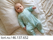 Cute Newborn Baby Lying on the Back in a Child Crib on White. Top View of Little Energetic Child. Playful Neonate Toddler Looks Around and Waving Hands. Concept of Childhood, New Life, Baby Care. Стоковое фото, фотограф Марина Демидюк / Фотобанк Лори