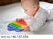 Happy Kid Playing with Pop It. Newborn Baby Playing with Simple Dimple. The Flexible Sensory Fidget Push-Bubble Toy is Good for Baby Development. Little Child Holds an Eternal Bubble in her Mouth. Стоковое фото, фотограф Марина Демидюк / Фотобанк Лори