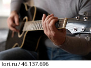 Playing the guitar. Strumming black acoustic guitar. Musician plays music. Man fingers holding mediator. Male hand playing guitar neck in dark room. Unrecognizable person rehearsing, fretboard closeup. Стоковое фото, фотограф Марина Демидюк / Фотобанк Лори