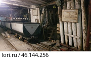 An old mine in Vorkuta, with narrow mine tracks with loaded mine cars on them. You can see the wooden logs that support the tunnel. The walls and ceiling of the mine are dark, covered with soot and traces of dampness, creating the atmosphere of an abandoned or museum object.On the right side there are signs, one of which is called "Mine cars", indicating the museum nature of the exhibition. Above the stairs there is a radiation sign, possibly warning of a possible danger. The stairs lead up into the depths of the tunnel, creating an effect of the unknown.Such mines were key coal mining sites in Vorkuta, playing an important role in the history of the city and the region. This is a reminder of the hard work of the miners, as well as the Gulag era, when prisoners worked in the mines. (2021 год). Редакционное фото, фотограф Анна Кривицкая / Фотобанк Лори
