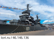 The cruiser "Mikhail Kutuzov", which is a museum ship in the city of Novorossiysk. This Project 68-bis warship was part of the USSR Navy for a long time, and then was turned into a museum, becoming one of the main attractions of the city.The side of the ship with the number "105", which indicates its affiliation with the Navy.You can see the flag garland - a ship decoration used during celebrations.Antennas and radar installations on the masts of the cruiser.A group of tourists on board, inspecting the ship.Mooring ropes secured to the pier.The protective paint of the hull is a characteristic dark gray color. (2023 год). Редакционное фото, фотограф Анна Кривицкая / Фотобанк Лори