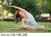 Woman practicing hatha yoga in garden, stretching in an asymmetrical seated asana Parivritta Janu Sirsasana. Стоковое фото, фотограф Яков Филимонов / Фотобанк Лори