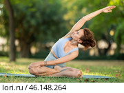 Woman practicing hatha yoga in garden, stretching in an asymmetrical seated asana Parivritta Janu Sirsasana. Стоковое фото, фотограф Яков Филимонов / Фотобанк Лори