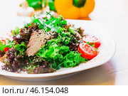 Fresh salad with greens, tomatoes, and a sprinkle of seeds on a wooden table in a bright cafe setting. Стоковое фото, фотограф Сергей Толмачёв / Фотобанк Лори